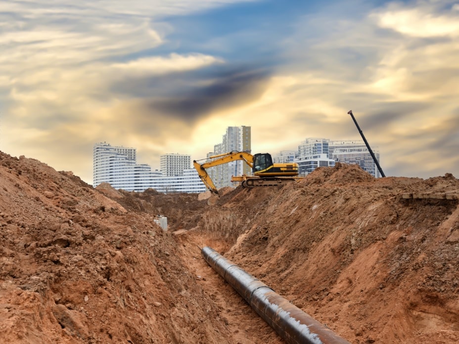 Excavator at construction site during laying sewer and main reticulation systems. Civil infrastructure pipe, water lines, sanitary sewers and storm sewers. Underground utilities-min