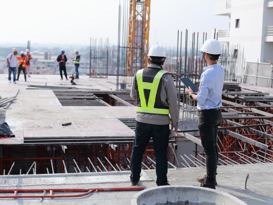 Two engineers work on the construction site. They are checking the progress of the work.-min